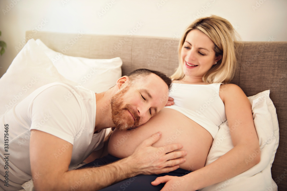 Beautiful pregnant woman and her handsome husband spending time together in bed ear belly Beautiful pregnant woman and her handsome husband spending time together in bed ear belly