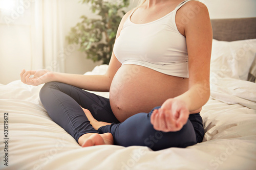 Pregnant woman doing yoga exercise on bed