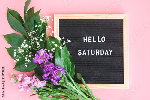 Hello Saturday text on black letter board and bouquet colorful flowers on pink background. Concept Happy Saturday. Template for postcard, greeting card Flat lay Top view photo