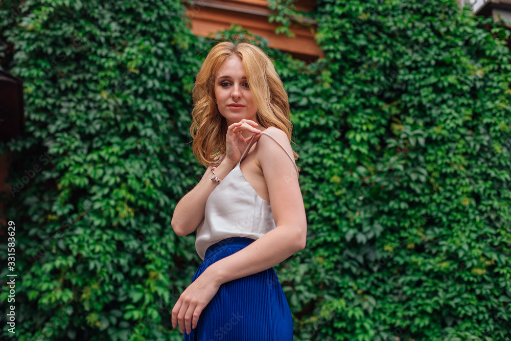 Portrait of a young beautiful woman, standing next to the wall of wild grape leaves holding a strap of a blouse. Portrait of a young beautiful woman, standing next to the wall of wild grape leaves holding a strap of a blouse.