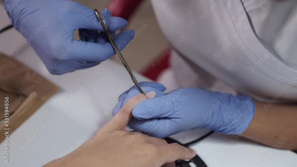 Master wears blue gloves. Nail artist uses scissors. Manicurist makes manicure for female client. Master wears blue gloves. Nail artist uses scissors. Manicurist makes manicure for female client.
