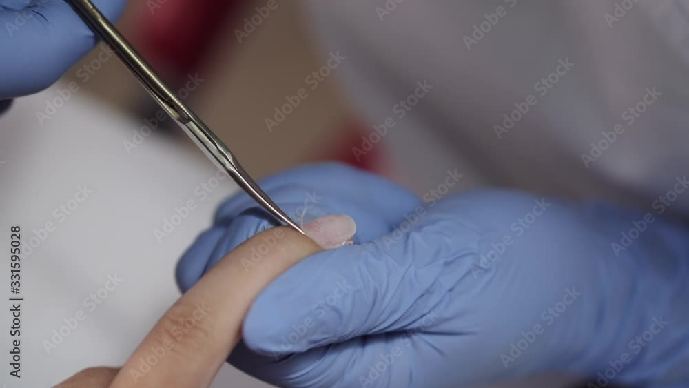 Master wears blue gloves. Nail artist uses scissors. Manicurist makes manicure for female client. Master wears blue gloves. Nail artist uses scissors. Manicurist makes manicure for female client.