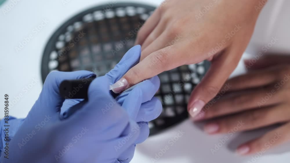Master wears blue gloves. Nail artist puts nail gel. Manicurist makes manicure for female client. Master wears blue gloves. Nail artist puts nail gel. Manicurist makes manicure for female client.