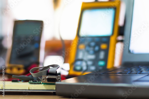 profesional technician measuring the small electronics device with digital multimeter, with blurry computer monitor in background, concept of modern repair shop.