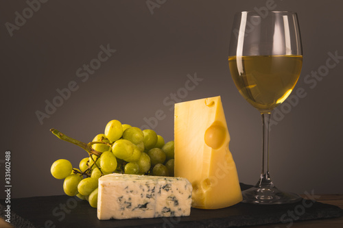 Glass of white wine. Still life with white grapes  Swiss and Blue cheese on slate board.  