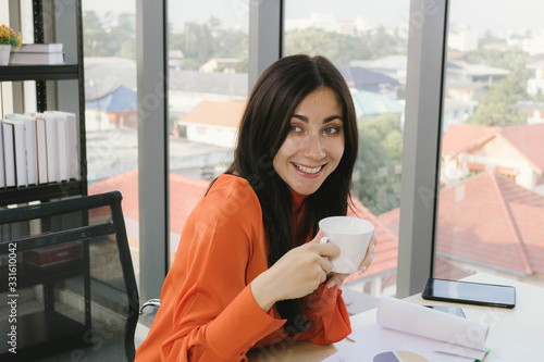 Young attractive business woman drinking coffe at her desk and feeling happy.
