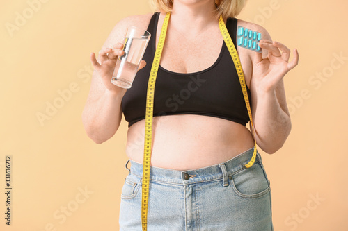 Woman with weight loss pills and measuring tape on color background photo