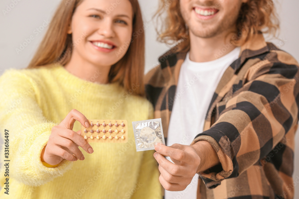 Young couple with birth control pills and condom on light background Young couple with birth control pills and condom on light background