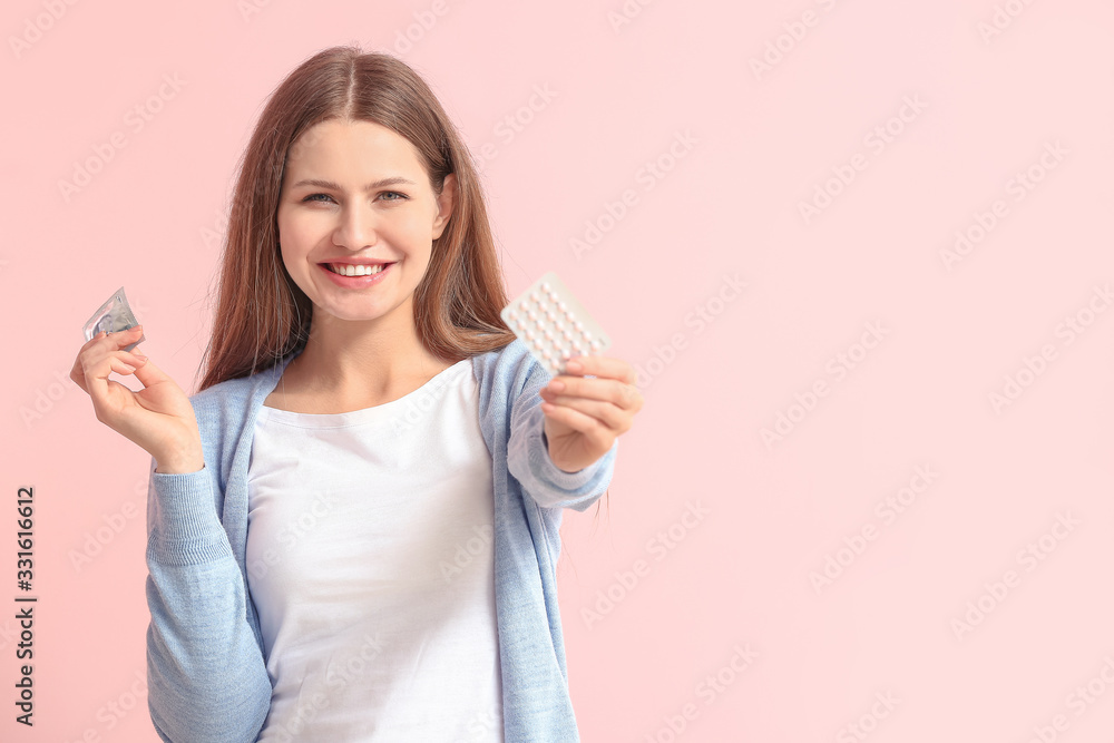 Young woman with birth control pills and condom on color background Young woman with birth control pills and condom on color background