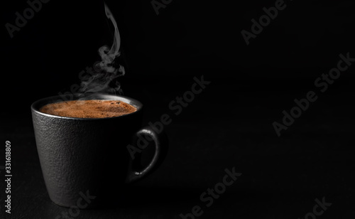A cup of espresso with foam, steam rises above a cup of coffee. Black stone background. Copy space for text. Close-up, shallow depth of field. Morning hours waiting for coffee.