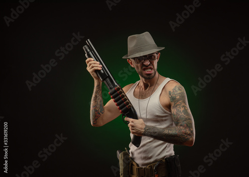an athletic guy with a tattoo poses with a shotgun