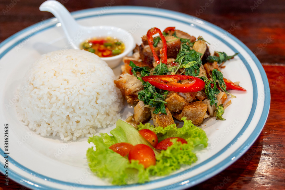 Delicious Crispy roasted pork stir fried with chili and basil leaf. Rice on white plate with pork chili basil. Delicious Crispy roasted pork stir fried with chili and basil leaf. Rice on white plate with pork chili basil.