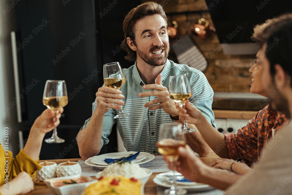 Young man proposing a toast while having lunch with friends at home.