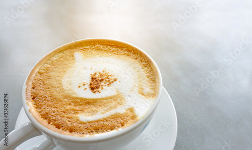 Tasty drinking, a cup of capuccino coffee decorated with fluffy white and brown milk froth in white ceramic cup on gray table, closeup photo