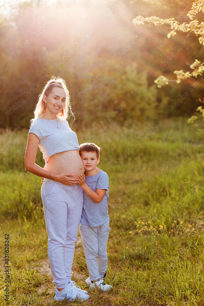 Fototapeta premium a child hugs the belly of a pregnant woman in the summer in a Park