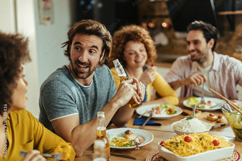 Happy man drinking beer and talking with friends while having lunch at home.