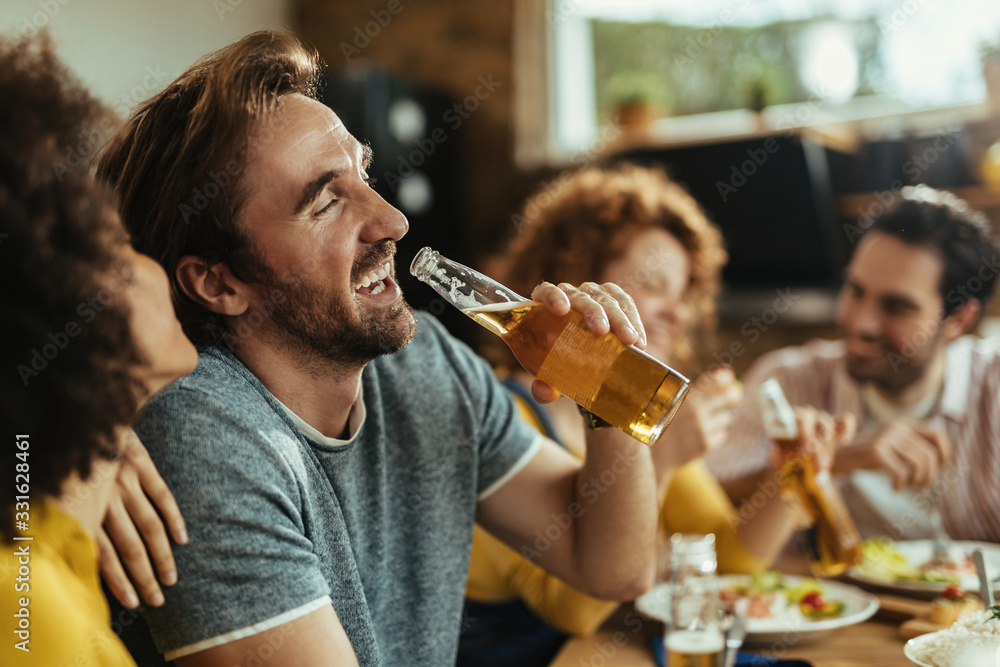 Cheerful man drinking beer while while having lunch with friends at home. Cheerful man drinking beer while while having lunch with friends at home.