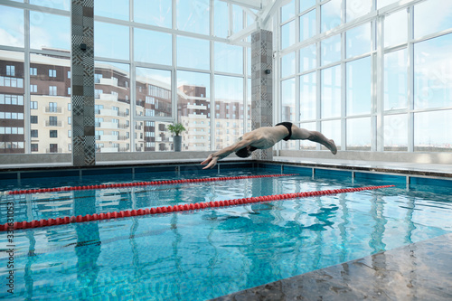 Athletic man jumping with raised arms in swimming pool, sporty man training in pool