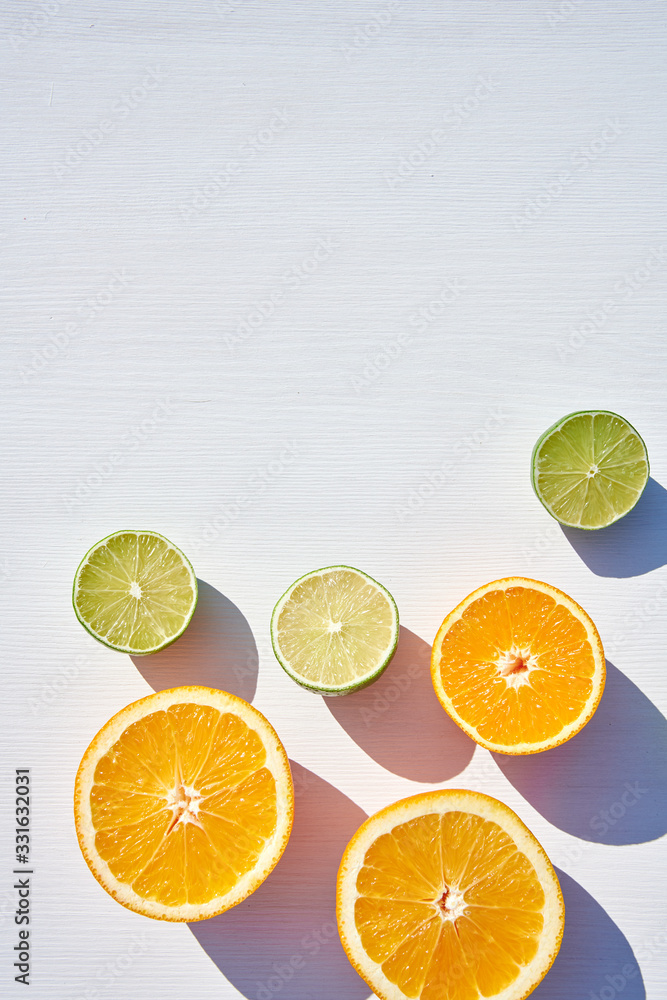 Ripe orange and lime halves on white wooden background, vertical shot from above in harsh sunlight with long colored shadows. A lot of background. Ripe orange and lime halves on white wooden background, vertical shot from above in harsh sunlight with long colored shadows. A lot of background.