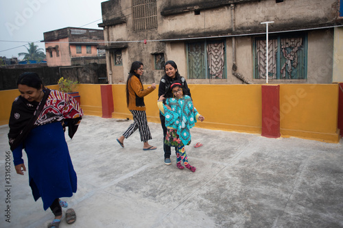Fototapeta Naklejka Na Ścianę i Meble -  A cheerful Indian Bengali family in winter garments enjoying in a sunny winter afternoon by playing football on a rooftop. Indian lifestyle.