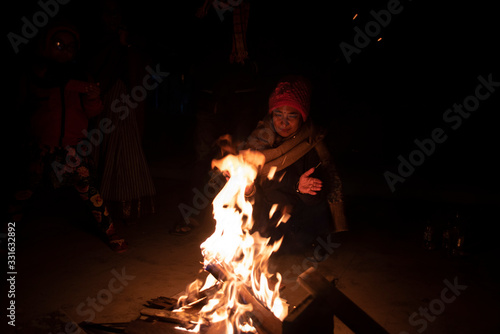 A cheerful Indian Bengali brunette family in winter wear enjoying bonfire on rooftop in the evening. Indian lifestyle and winter.