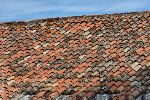 Pantiles. Closeup of a roof with new and old terracotta tiles (Coppo in Italian language), on a blue sky with clouds. Veneto, Italy, Europe