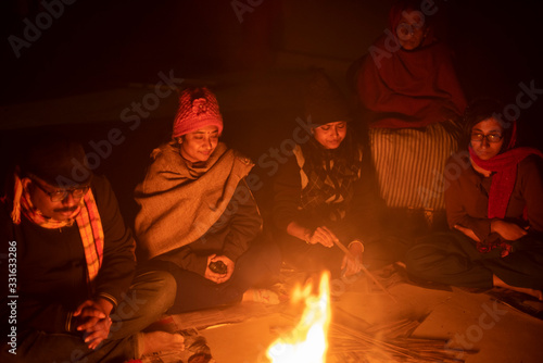 A cheerful Indian Bengali brunette family in winter wear enjoying bonfire  on rooftop in the evening. Indian lifestyle and winter.