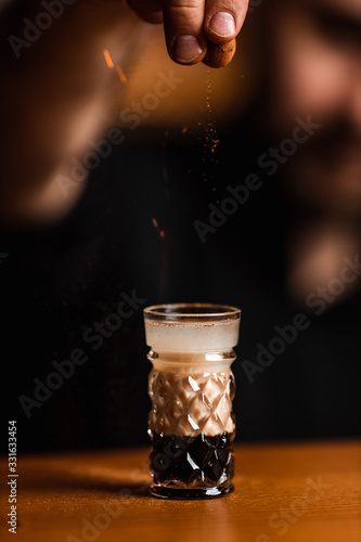 Professional bartender adding spices powder into a cocktail glass with strong alcoholic cocktail with coffee