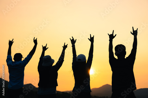 group of people with raised arms looking at sunrise on the mountain background. Happiness, success, friendship and community concepts.