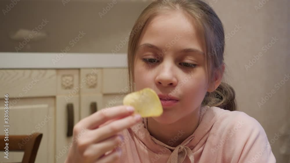 Beautiful teenage girl eating tasty chips at home. Close-up view of adorable happy teen girl enjoy eating crisps in kitchen Beautiful teenage girl eating tasty chips at home. Close-up view of adorable happy teen girl enjoy eating crisps in kitchen