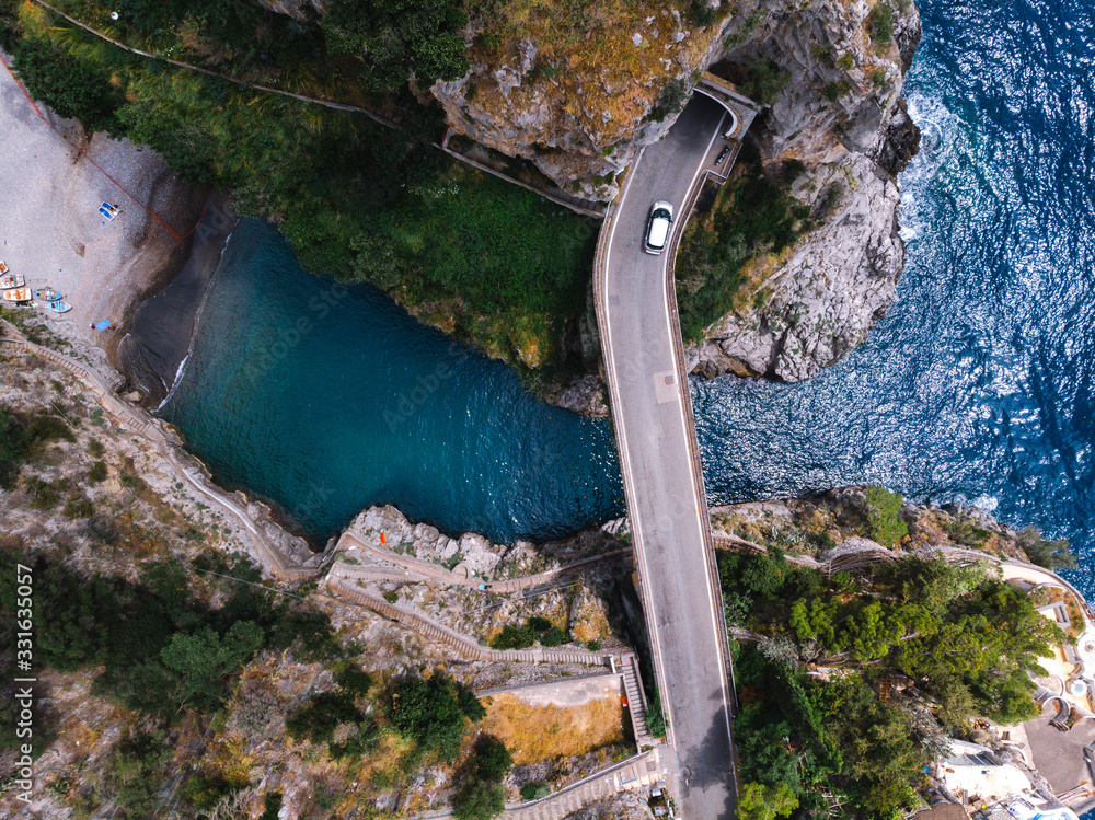 Obraz premium Aerial top down view of Fiordo di furore beach. Incredible beauty panorama of a paradise. The rocky seashore of southern Italy. Sunny summer day. Car ride on stone bridge and clear water. Amalfi coast