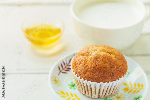 Close up banana cake on white plate with honey and cup of milk on wooden table.