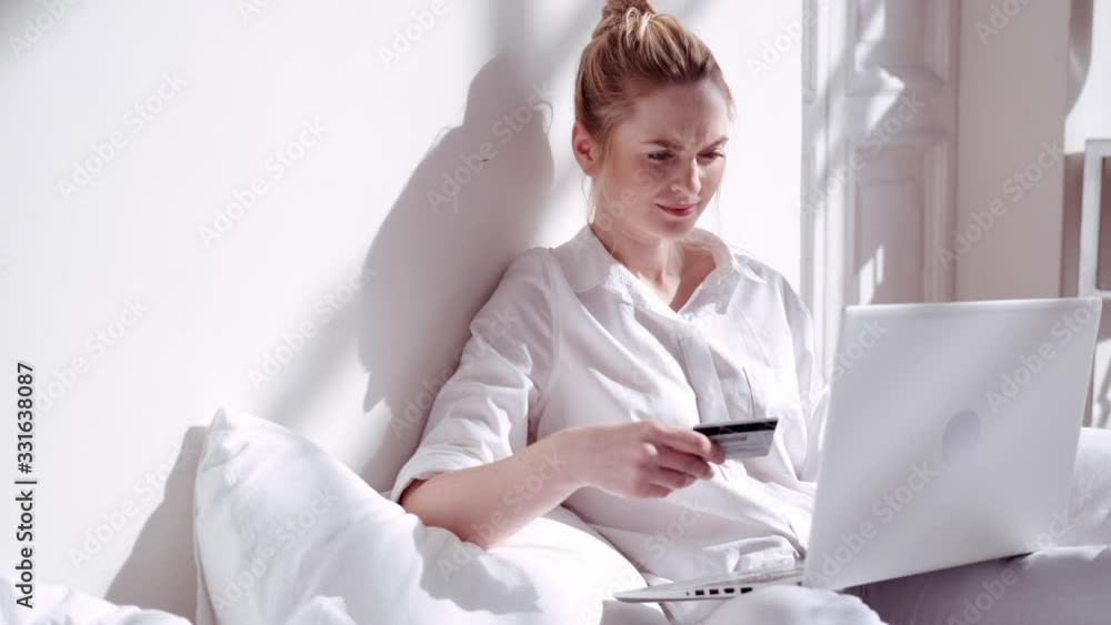 Modern woman makes an online purchase, staying in bed on sunny morning Modern woman makes an online purchase, staying in bed on sunny morning