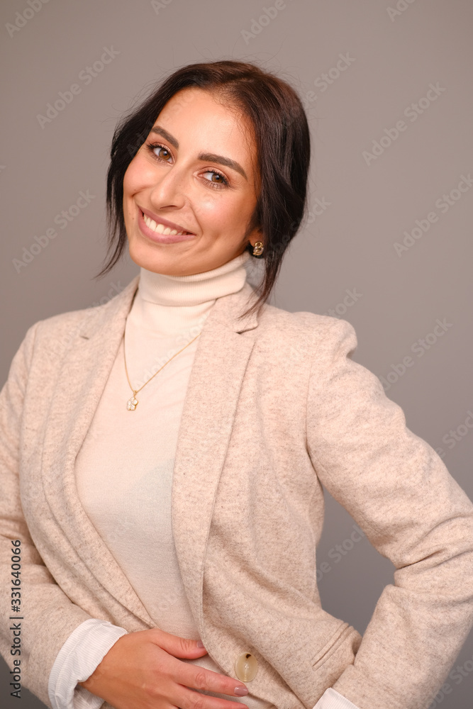Portrait of a smiling mid-aged business woman in a light milk-colored trouser suit and turtleneck against a light wall. Portrait of a smiling mid-aged business woman in a light milk-colored trouser suit and turtleneck against a light wall.