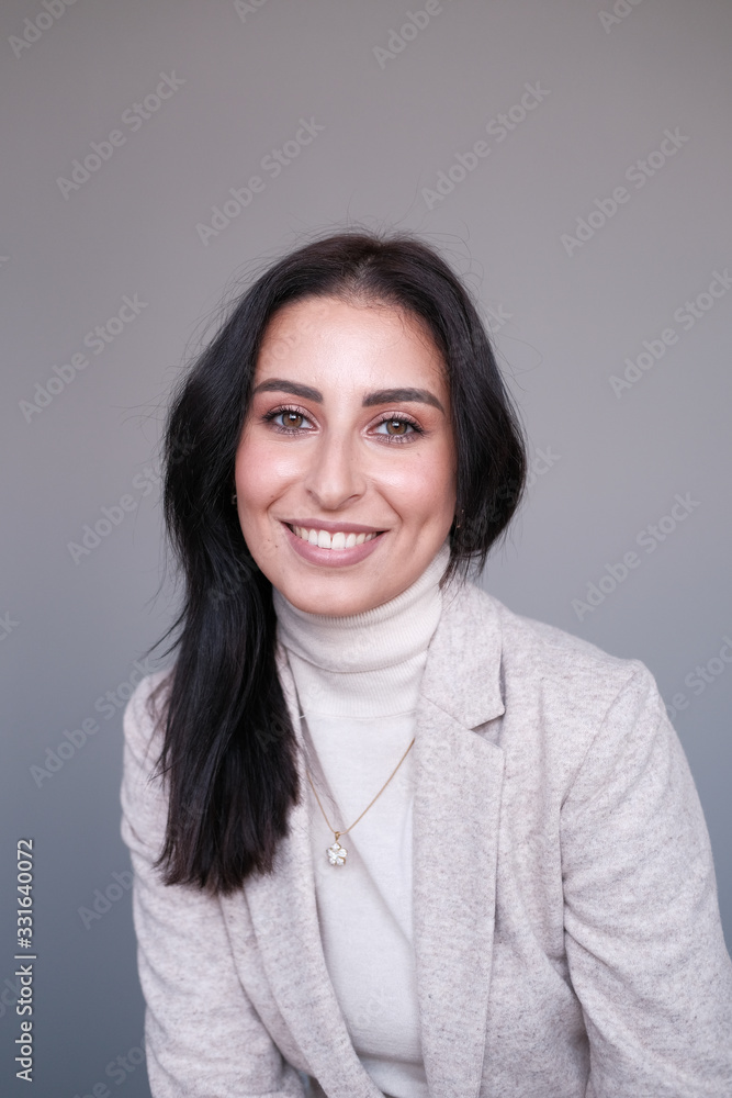 Portrait of a smiling mid-aged business woman in a light milk-colored trouser suit and turtleneck against a light wall. Portrait of a smiling mid-aged business woman in a light milk-colored trouser suit and turtleneck against a light wall.