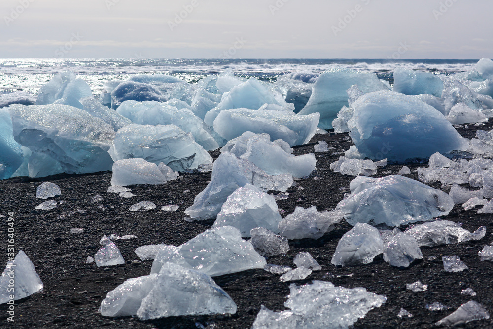 The block of ice is lying on the black volcanic sand on the The block of ice is lying on the black volcanic sand on the