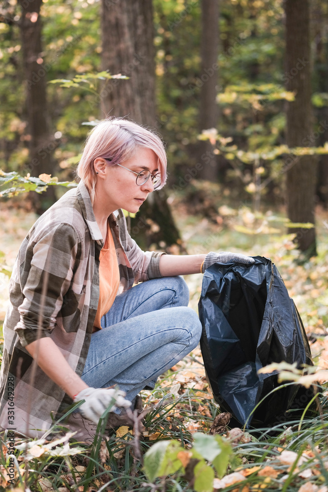 A young girl - an eco activist collects trash and plastic in a park and forest stacks up in a black big bag. Clean eco system concept A young girl - an eco activist collects trash and plastic in a park and forest stacks up in a black big bag. Clean eco system concept