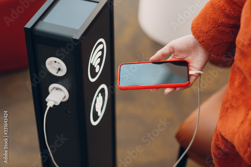 Canvas Print Woman holds mobile phone in her hand on background of  stand for charging and wi