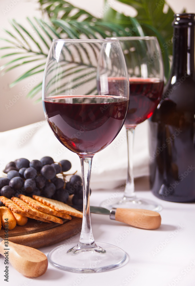 Two glass of red wine and plate with assorted cheese, fruit and other snacks for party