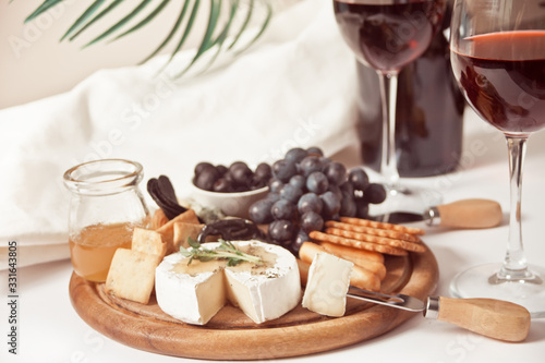 Two glass of red wine and plate with assorted cheese, fruit and other snacks for party