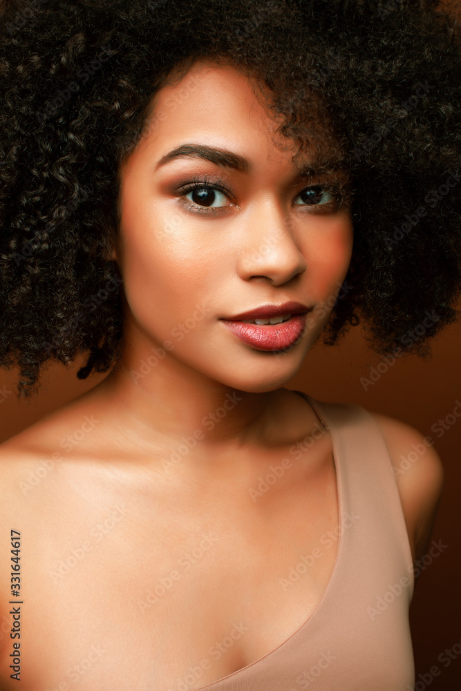 pretty young african american woman with curly hair posing cheerful gesturing on brown background, lifestyle people concept pretty young african american woman with curly hair posing cheerful gesturing on brown background, lifestyle people concept