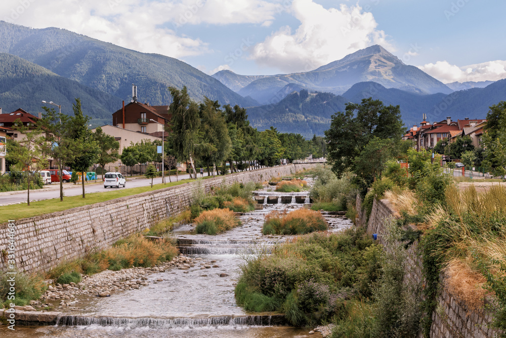 Fototapeta premium View of Bansko town, bulgarian ski resort in summer, Pirin Mountains in the background, a river in the foreground, Bulgaria.