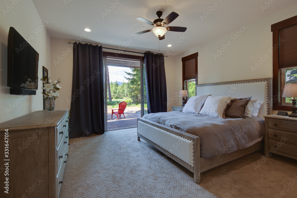 Fototapeta premium Beautiful large luxury new bedroom with great design, beige, grey and white tones, TV bove dresser, rich wooden doors, window blinds and grey carpet. Cozy and practicle. Expensive furniture.