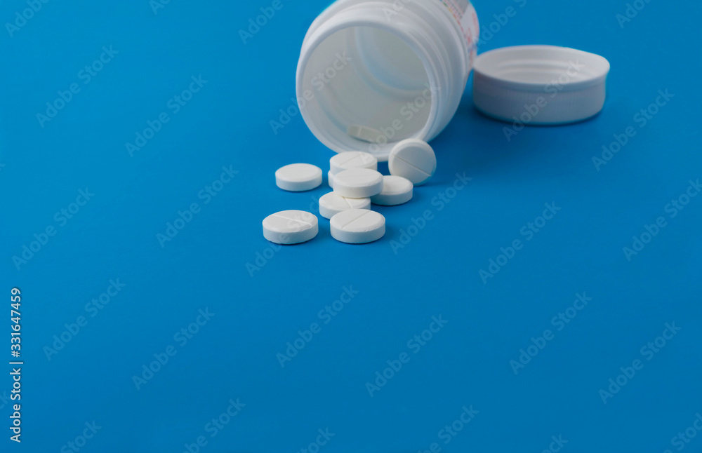 white tablets in a plastic jar with a lid, lying on an isolated blue background
