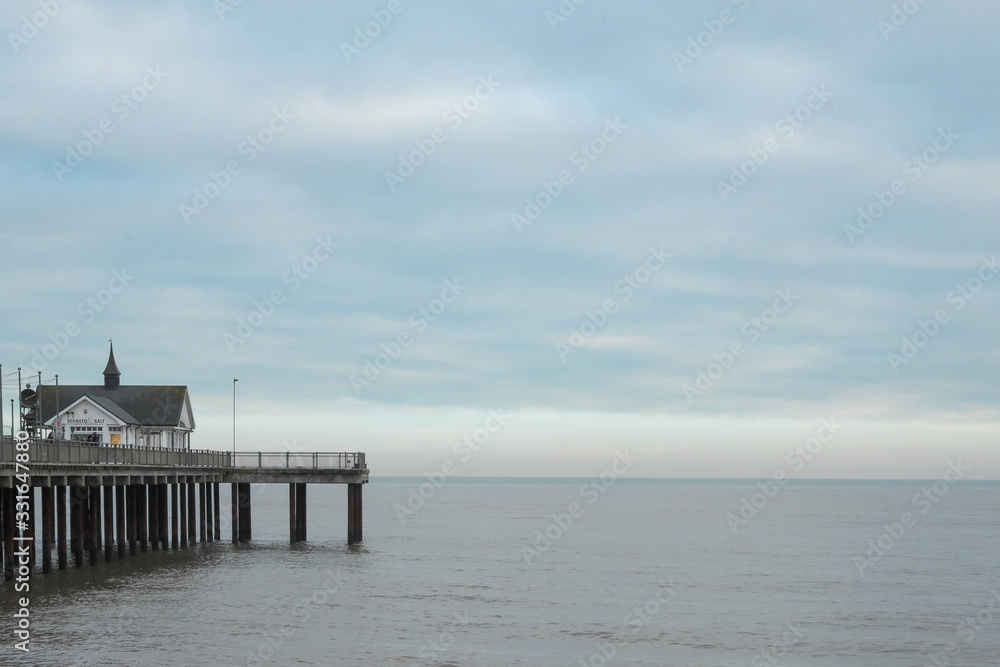 El final del muelle de Southwold con un cielo nuboso, la linea del horizonte con luz y el mar gris