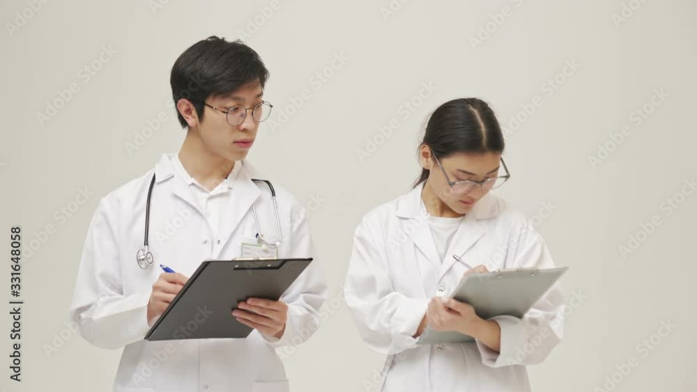 Young asian concentrated doctors isolated over white background in sterile uniform writing notes in clipboard Young asian concentrated doctors isolated over white background in sterile uniform writing notes in clipboard