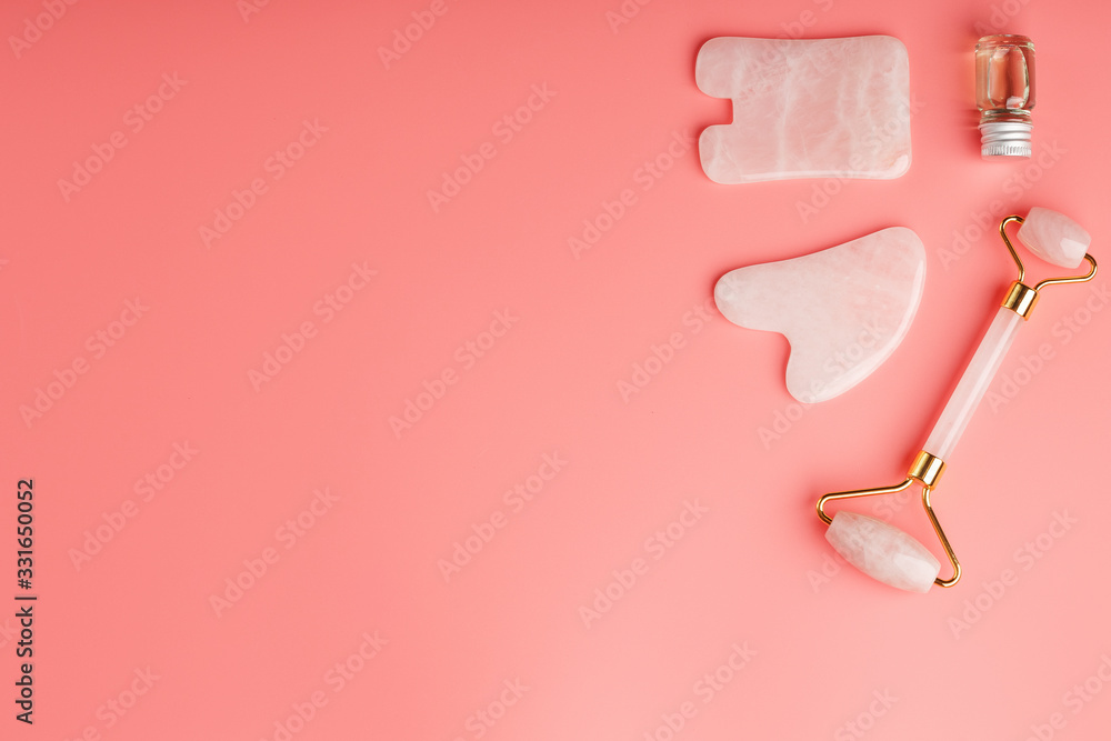 A set of tools for face Massage technique Gua Sha made of natural rose quartz on a pink background. Roller, jade stone and oil in a glass jar for face and body care. A set of tools for face Massage technique Gua Sha made of natural rose quartz on a pink background. Roller, jade stone and oil in a glass jar for face and body care.