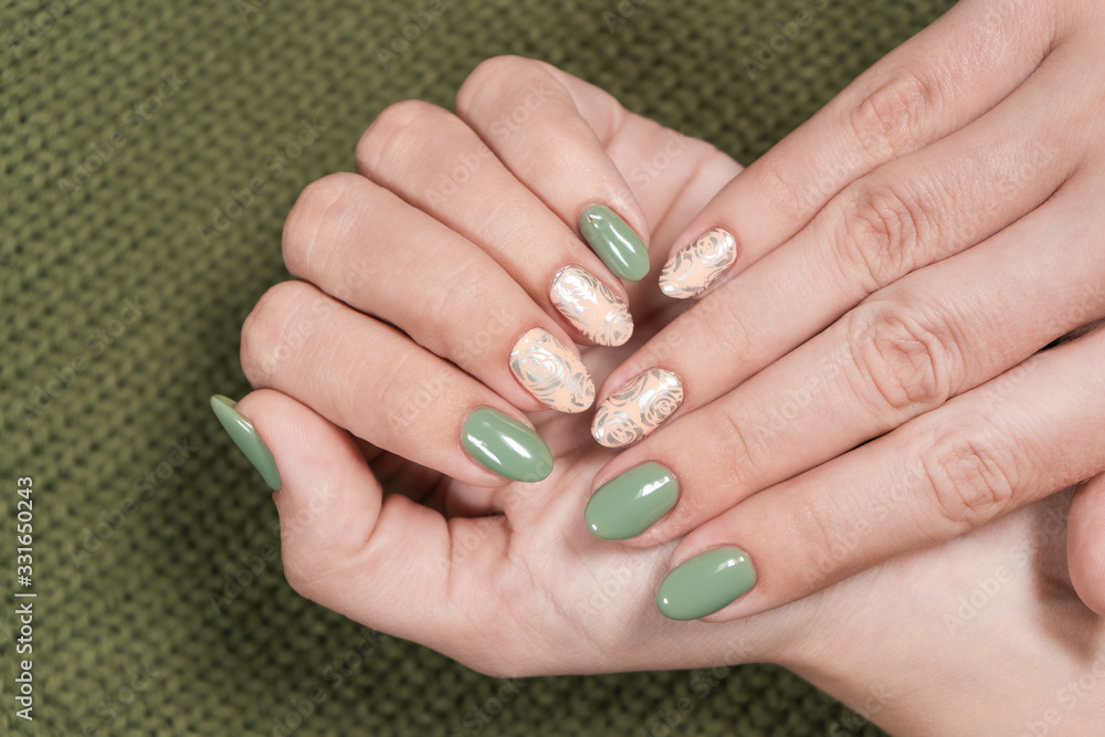 Closeup top view of two beautiful female hands of white woman with fresh modern stylish manicure of green and beige pastel colors. Hands isolated on green knitted texture background. Closeup top view of two beautiful female hands of white woman with fresh modern stylish manicure of green and beige pastel colors. Hands isolated on green knitted texture background.