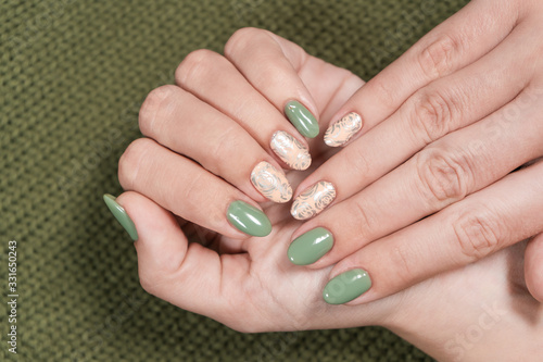 Closeup top view of two beautiful female hands of white woman with fresh modern stylish manicure of green and beige pastel colors. Hands isolated on green knitted texture background. 