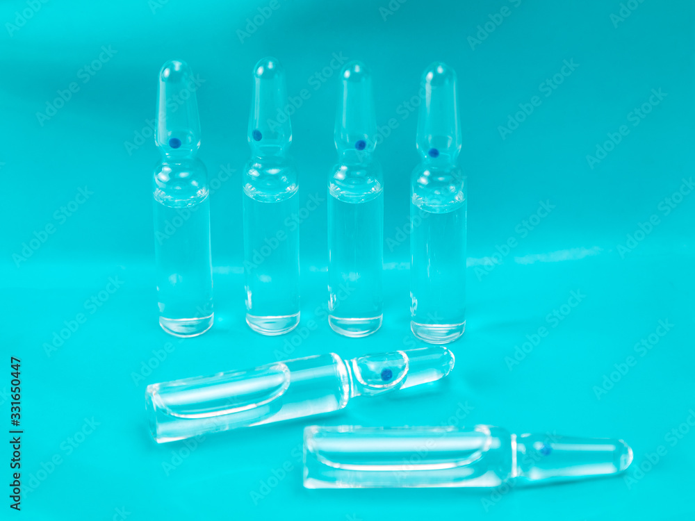 Glass ampoules with medicine on a blue background. The rear row of ampoules stands in the row, with two pieces lying in the foreground. The place for an inscription